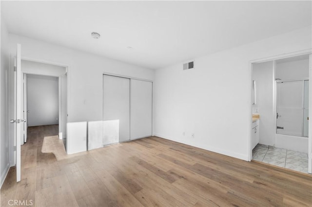 unfurnished bedroom featuring a closet, ensuite bathroom, and light hardwood / wood-style flooring