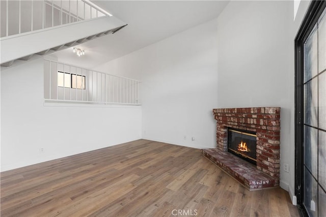 unfurnished living room featuring a brick fireplace, a towering ceiling, and hardwood / wood-style flooring