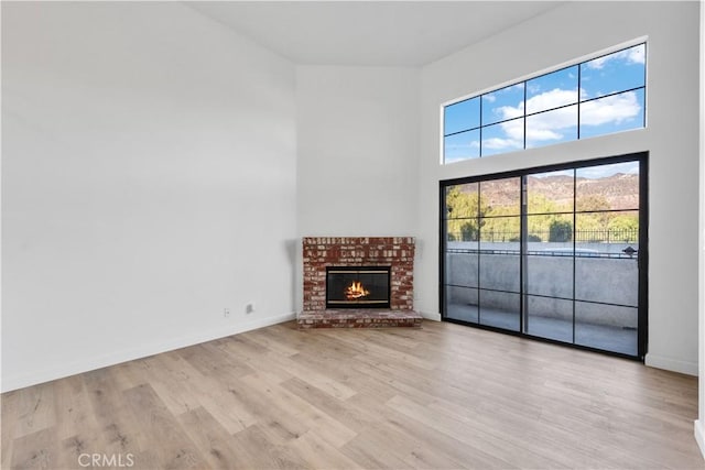 unfurnished living room with a brick fireplace, a towering ceiling, light hardwood / wood-style flooring, and a wealth of natural light