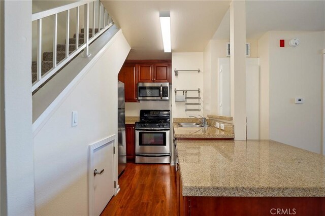 kitchen featuring appliances with stainless steel finishes, light stone counters, dark wood-type flooring, and sink