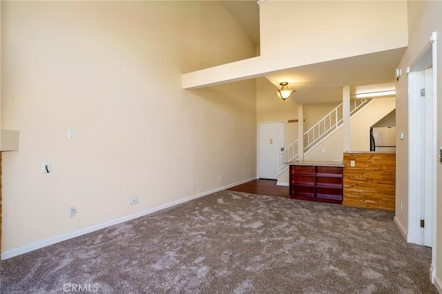 unfurnished living room with dark colored carpet and a high ceiling