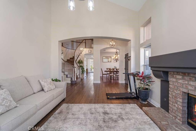 living room featuring dark hardwood / wood-style floors, an inviting chandelier, high vaulted ceiling, and a brick fireplace