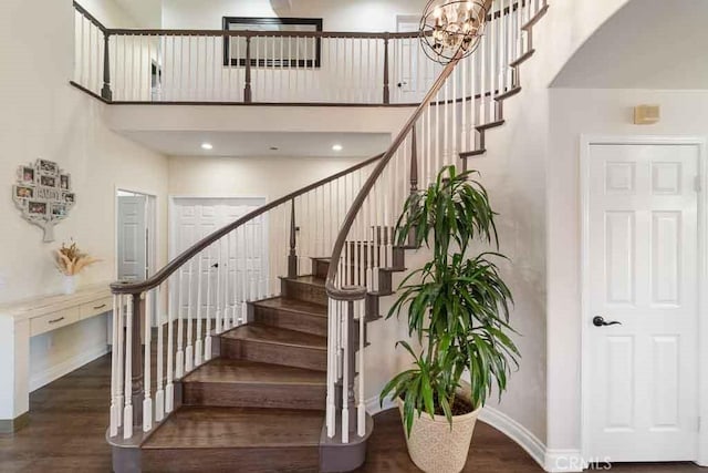 stairway with a chandelier, hardwood / wood-style floors, and a towering ceiling