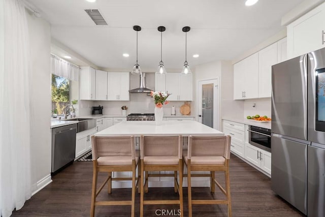 kitchen featuring stainless steel appliances, sink, wall chimney range hood, pendant lighting, and a center island