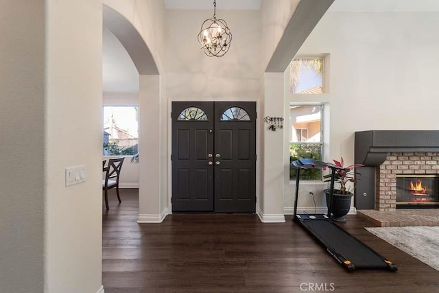 entryway with dark hardwood / wood-style floors, a towering ceiling, a fireplace, and a chandelier