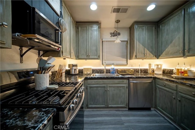 kitchen with sink, dark stone counters, hanging light fixtures, and stainless steel appliances