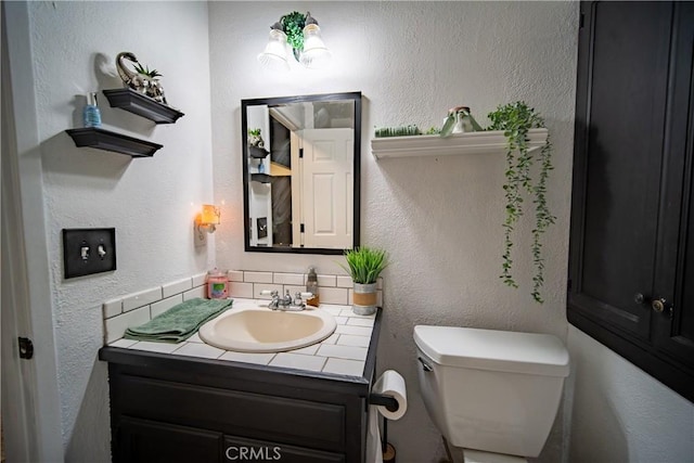 bathroom with toilet, vanity, and tasteful backsplash