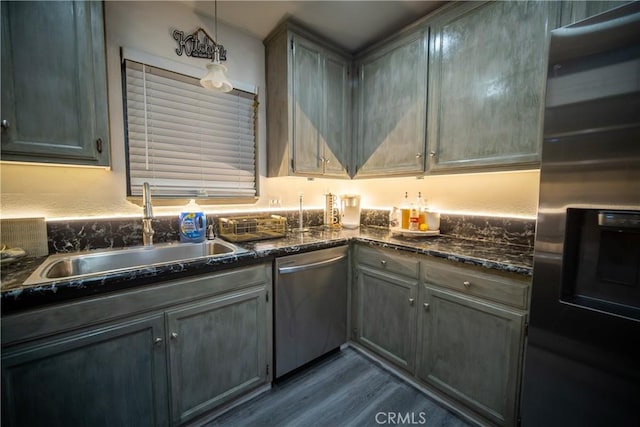 kitchen with wood-type flooring, stainless steel appliances, dark stone counters, sink, and hanging light fixtures