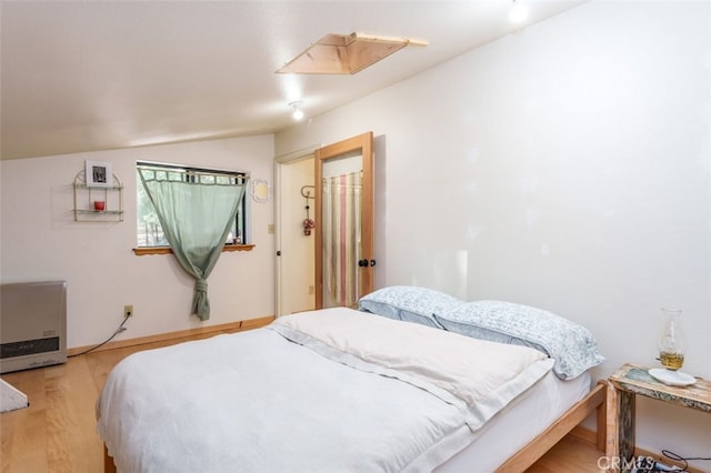 bedroom featuring heating unit, a closet, light hardwood / wood-style floors, and lofted ceiling