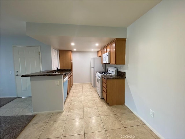 kitchen with sink, kitchen peninsula, dark stone countertops, white appliances, and light tile patterned floors