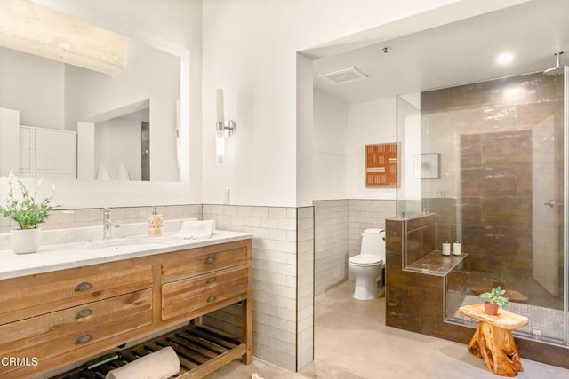 bathroom featuring vanity, toilet, tiled shower, tile walls, and concrete flooring