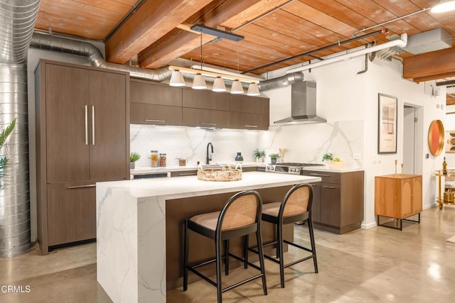 kitchen featuring wooden ceiling, wall chimney range hood, sink, a kitchen island, and a breakfast bar area