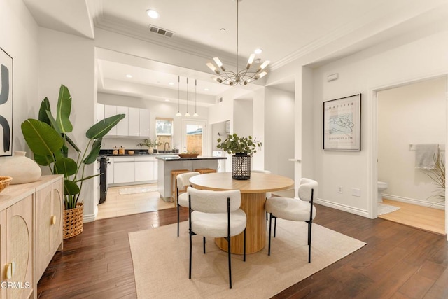 dining room with a notable chandelier, sink, dark wood-type flooring, and crown molding