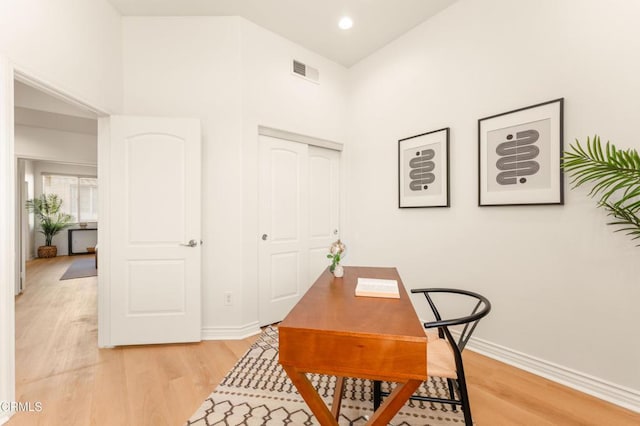 home office with a high ceiling and light hardwood / wood-style flooring