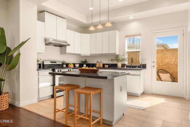 kitchen with white cabinetry, a kitchen island, range with gas stovetop, and light wood-type flooring