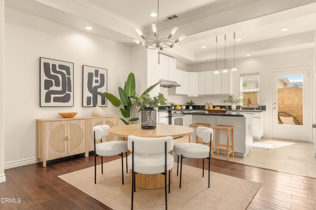 dining space featuring a raised ceiling, sink, dark hardwood / wood-style floors, ornamental molding, and a notable chandelier