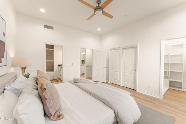 bedroom with ceiling fan, ensuite bathroom, a walk in closet, a closet, and light wood-type flooring