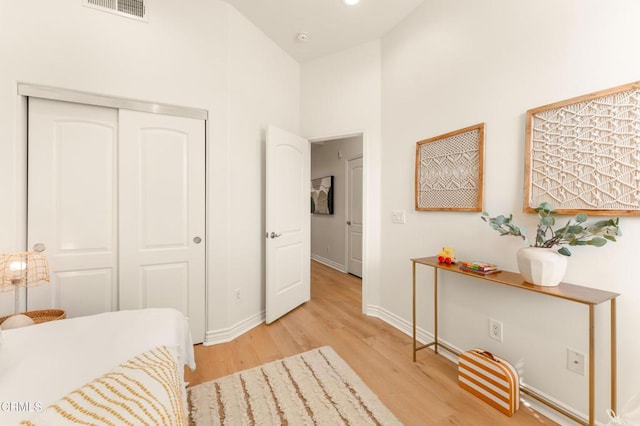 bedroom featuring light hardwood / wood-style floors, high vaulted ceiling, and a closet