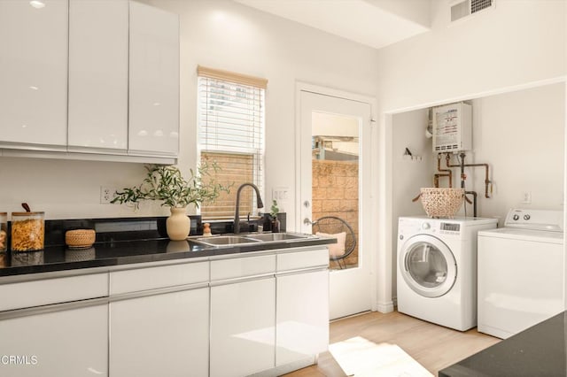 washroom featuring cabinets, sink, washing machine and dryer, light wood-type flooring, and water heater