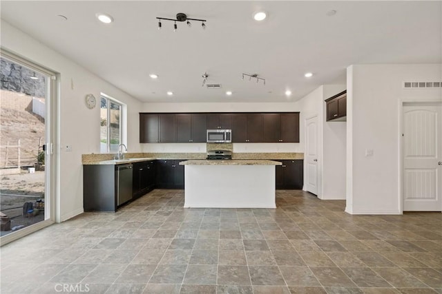 kitchen featuring sink, appliances with stainless steel finishes, dark brown cabinetry, light stone countertops, and a kitchen island