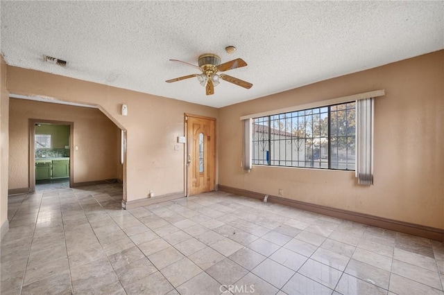 tiled empty room with ceiling fan and a textured ceiling