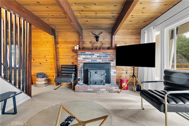 carpeted living room with a wood stove, wooden walls, beamed ceiling, and wood ceiling