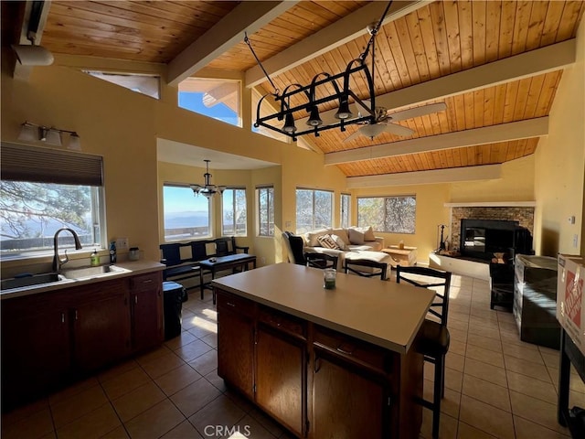 kitchen featuring vaulted ceiling with beams, a stone fireplace, dark brown cabinets, and sink