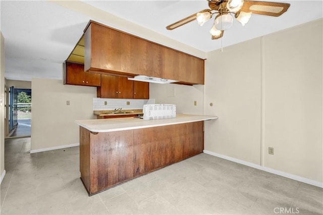 kitchen featuring kitchen peninsula, backsplash, ceiling fan, and sink