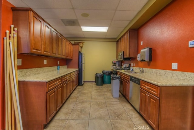 kitchen featuring light stone countertops, a drop ceiling, stainless steel appliances, sink, and light tile patterned floors