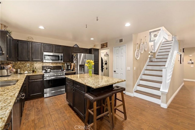 kitchen with decorative backsplash, appliances with stainless steel finishes, a kitchen breakfast bar, light stone counters, and wood-type flooring