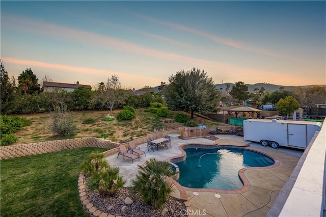 pool at dusk featuring a patio area, a mountain view, and a yard