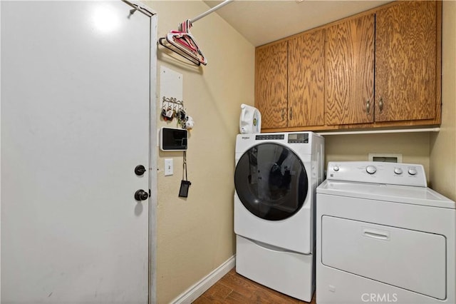 laundry room with washing machine and clothes dryer, dark wood-type flooring, and cabinets