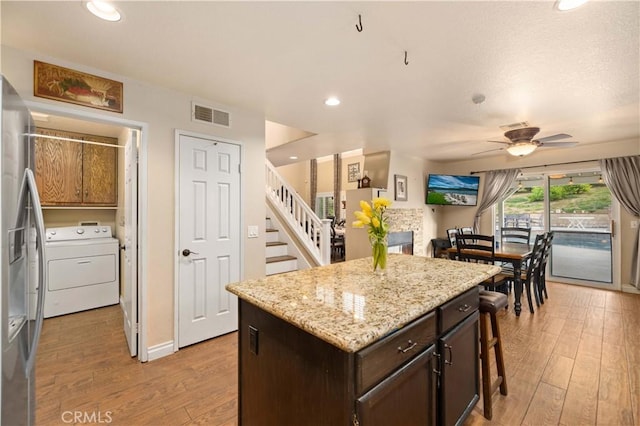 kitchen featuring ceiling fan, light wood-type flooring, dark brown cabinets, washer / dryer, and stainless steel refrigerator