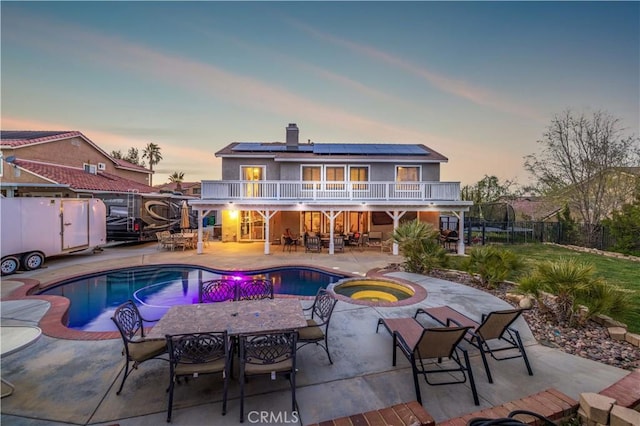 pool at dusk with a patio area and an in ground hot tub