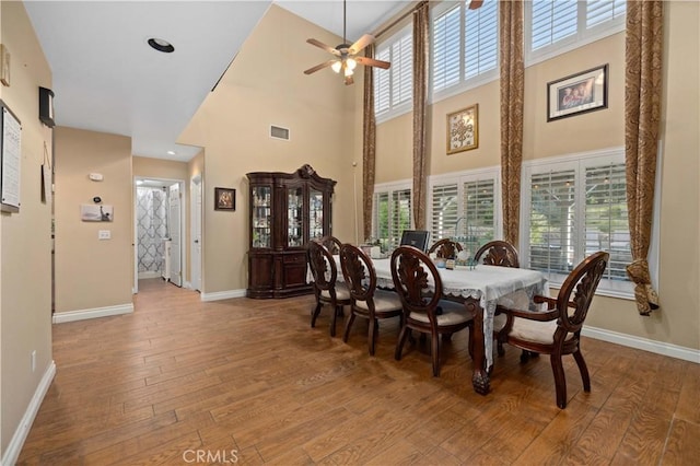 dining space with a high ceiling, ceiling fan, and wood-type flooring