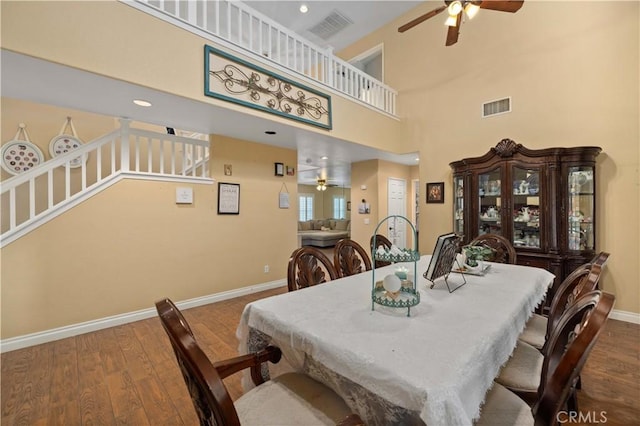 dining room with hardwood / wood-style floors, ceiling fan, and a towering ceiling