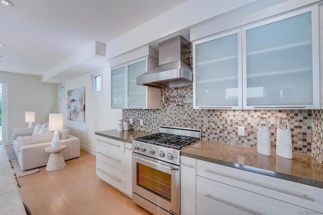 kitchen featuring white cabinets, high end stainless steel range oven, wall chimney exhaust hood, decorative backsplash, and light hardwood / wood-style floors