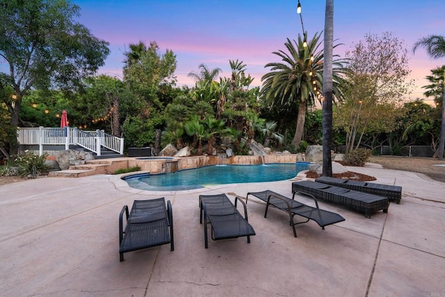 pool at dusk with a patio area and an in ground hot tub