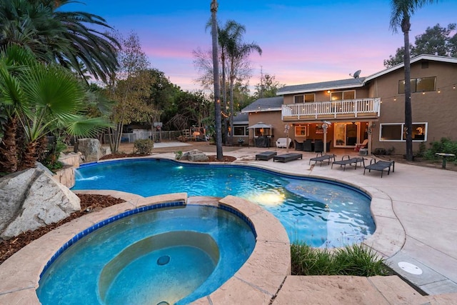 pool at dusk with pool water feature, a patio area, and an in ground hot tub