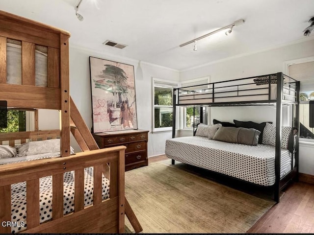 bedroom featuring hardwood / wood-style flooring, track lighting, and ornamental molding