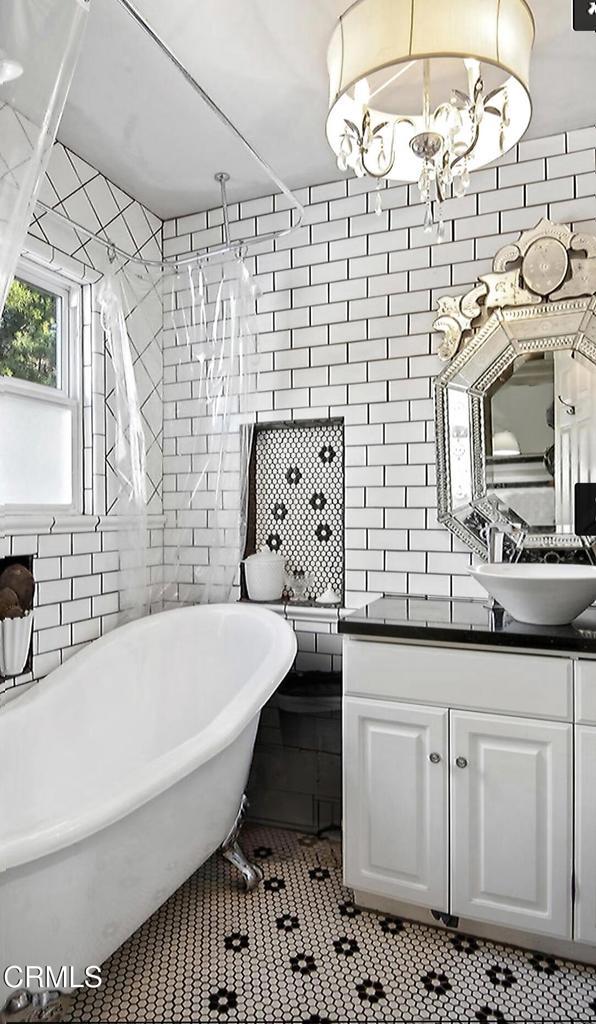 bathroom with vanity, a tub to relax in, tile walls, and an inviting chandelier