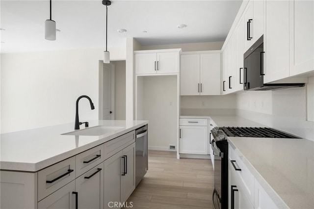 kitchen with sink, hanging light fixtures, light wood-type flooring, white cabinetry, and stainless steel appliances