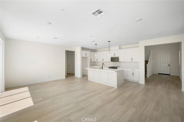 kitchen featuring white cabinetry, sink, hanging light fixtures, a center island with sink, and light wood-type flooring