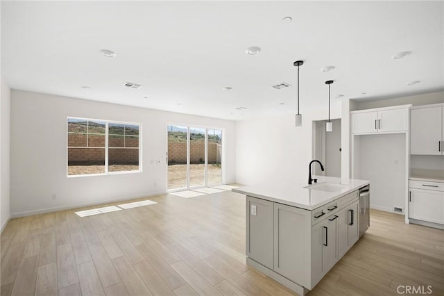 kitchen featuring a kitchen island with sink, sink, light hardwood / wood-style flooring, white cabinets, and hanging light fixtures