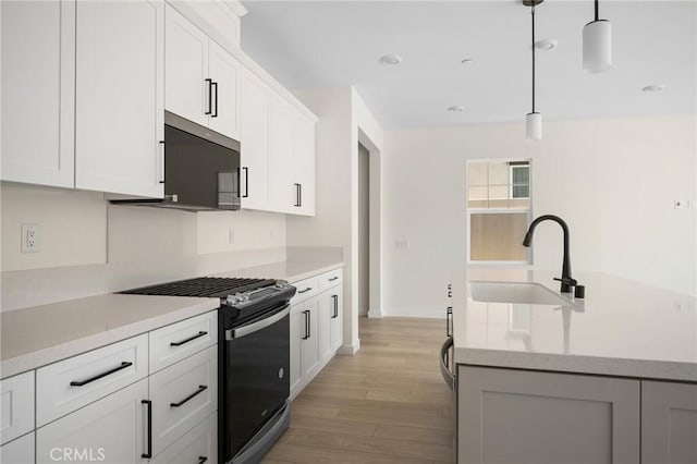 kitchen featuring white cabinetry, sink, light hardwood / wood-style floors, decorative light fixtures, and appliances with stainless steel finishes