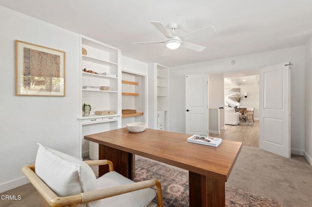 office space featuring baseboards, a ceiling fan, and light colored carpet