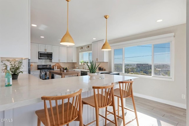 kitchen with backsplash, stainless steel microwave, black gas range oven, and a peninsula