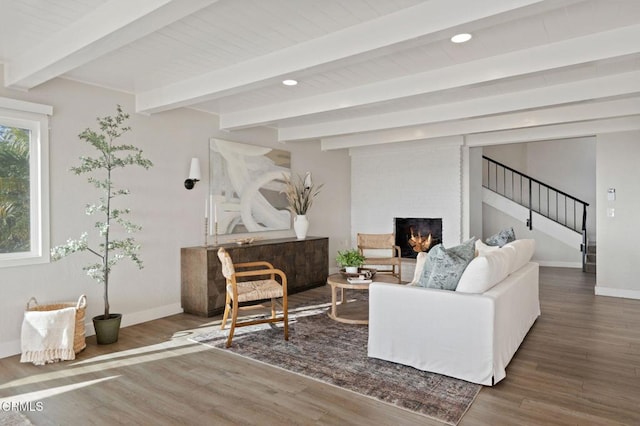 living area featuring beamed ceiling, a brick fireplace, wood finished floors, and baseboards