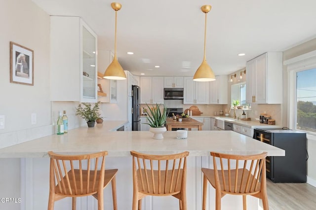 kitchen featuring a peninsula, a sink, white cabinets, light countertops, and appliances with stainless steel finishes