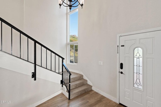 foyer featuring wood finished floors, a towering ceiling, baseboards, stairs, and an inviting chandelier